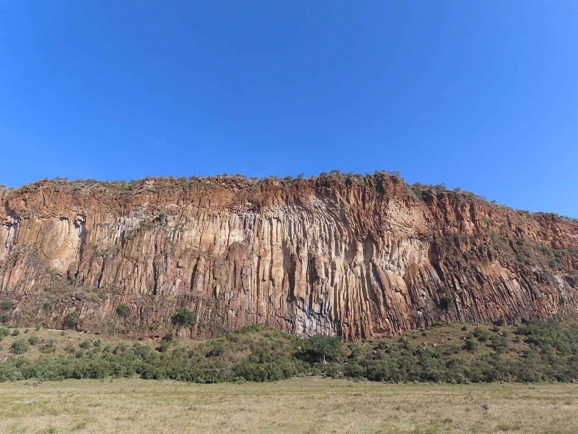 Tall red-brown volcanic cliffs under a clear blue sky in Hell's Gate National Park