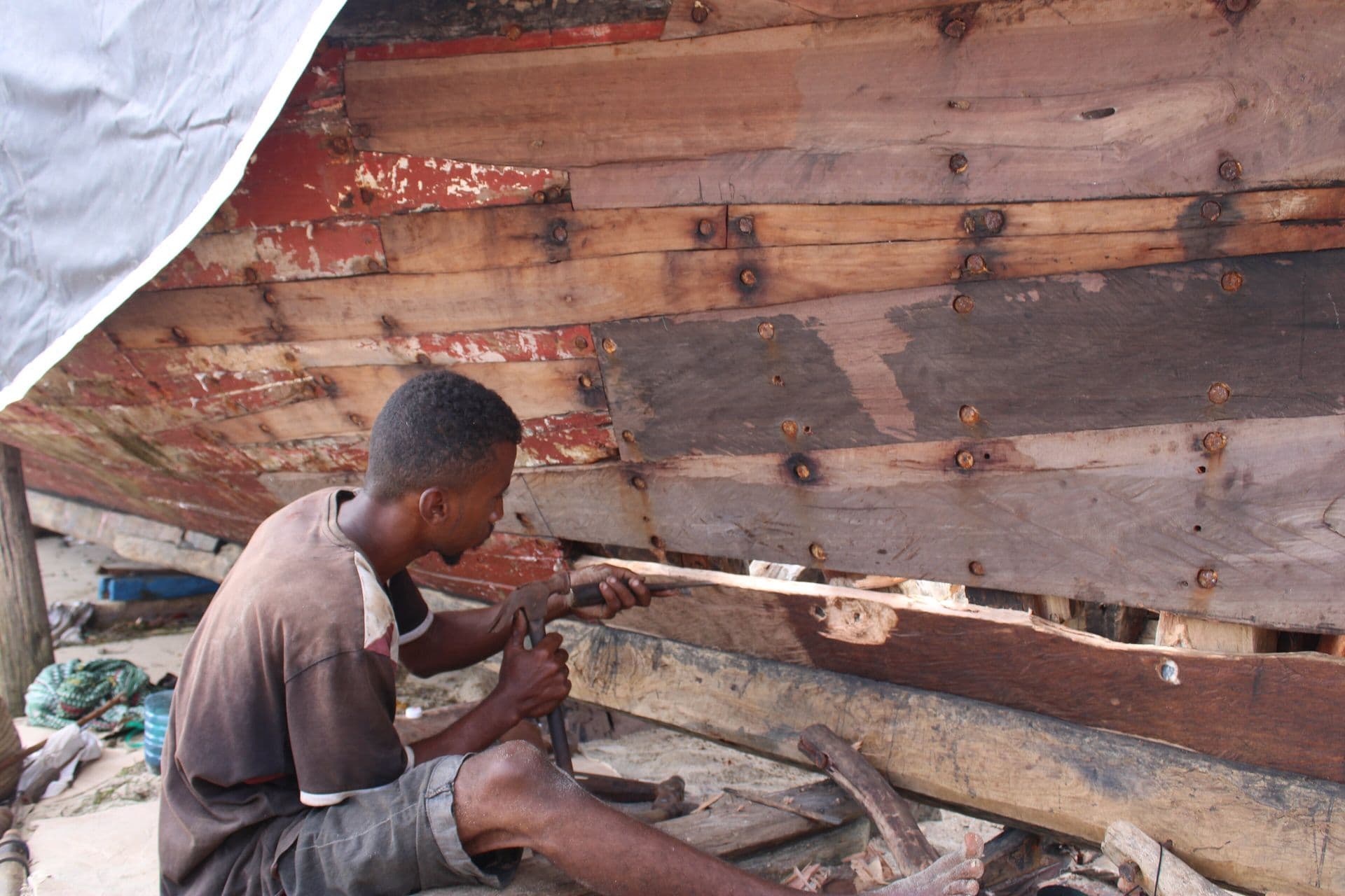 A craftsman shaping the wooden planks of a dhow hull under construction