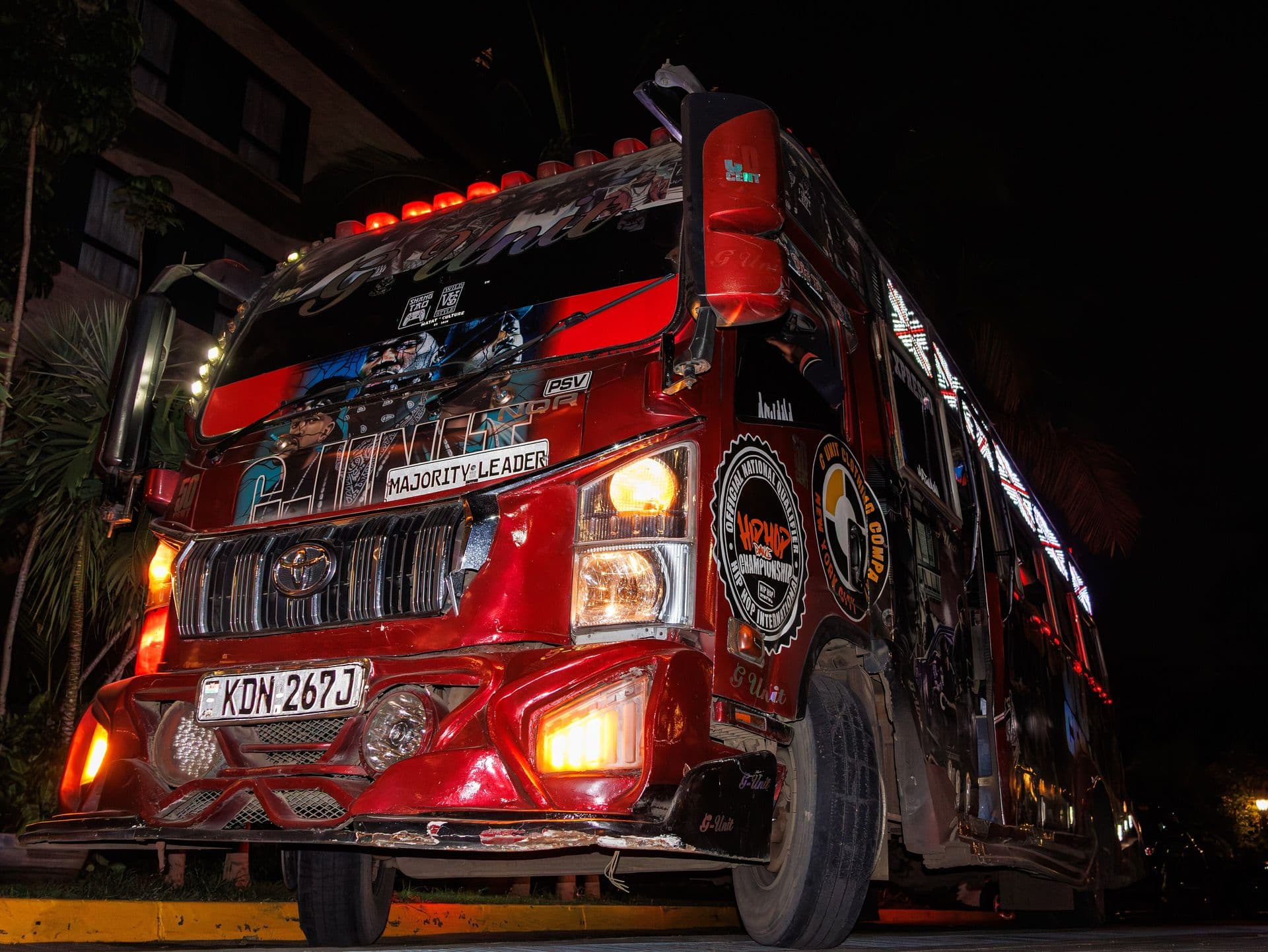 A red matatu with lit-up artwork and chrome detailing, photographed at night
