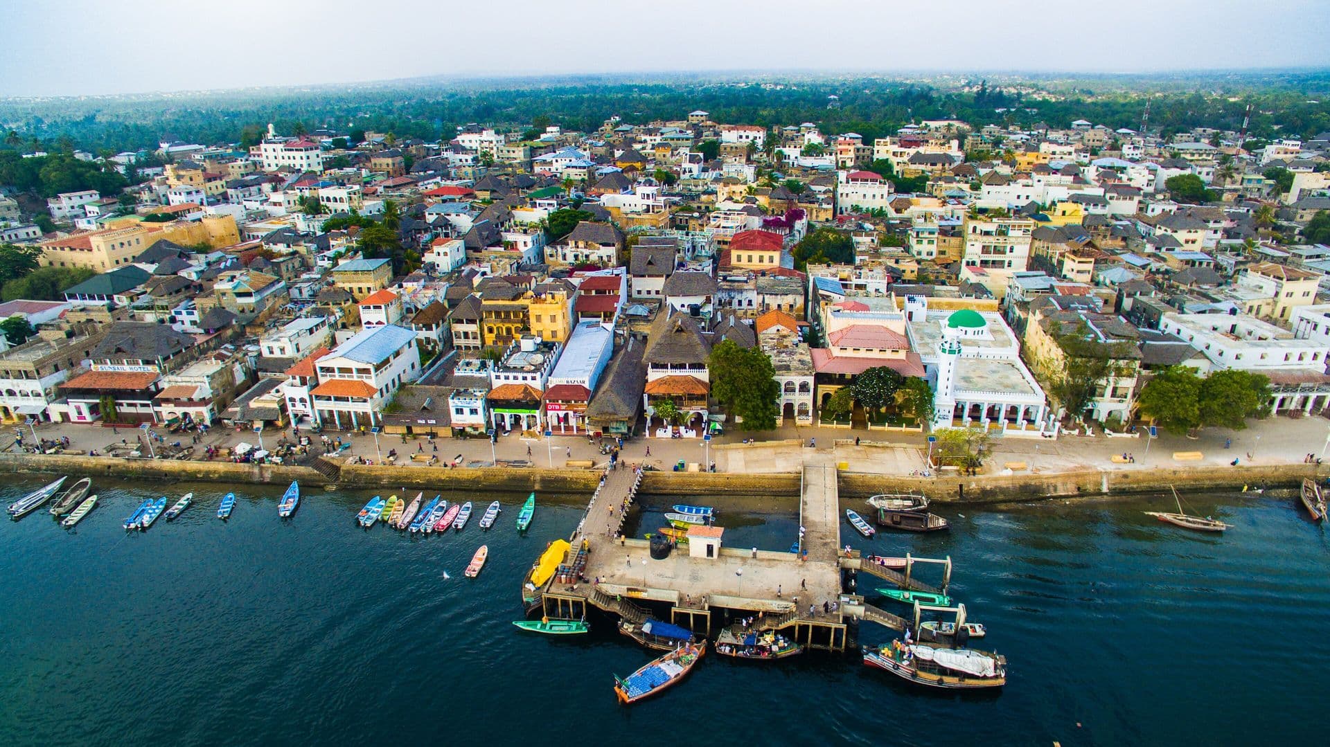 Aerial view of Lamu town's tightly packed buildings along the waterfront, with boats moored at the jetties