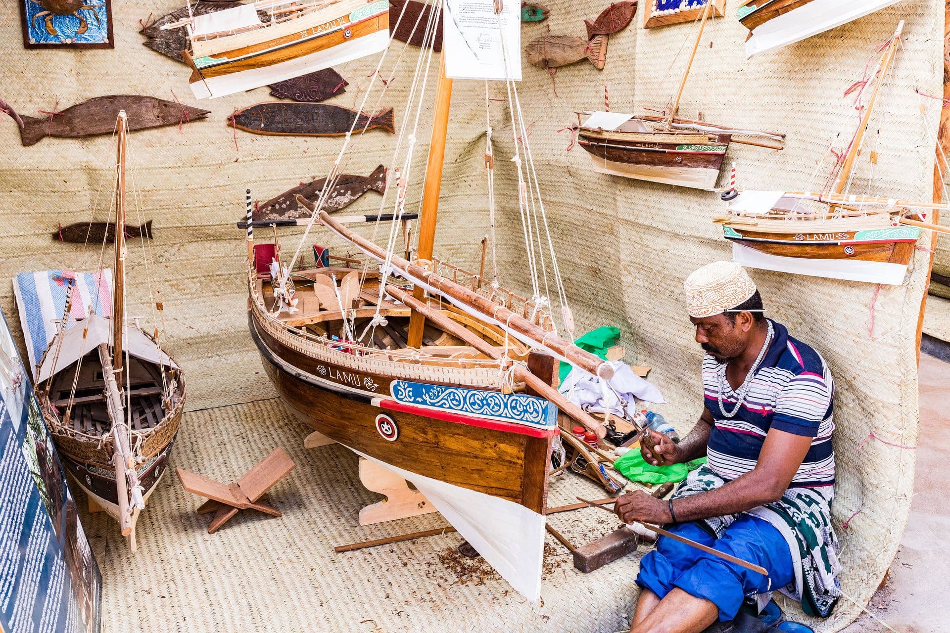 A craftsman in a kofia working among carved wooden model dhows in a Lamu workshop