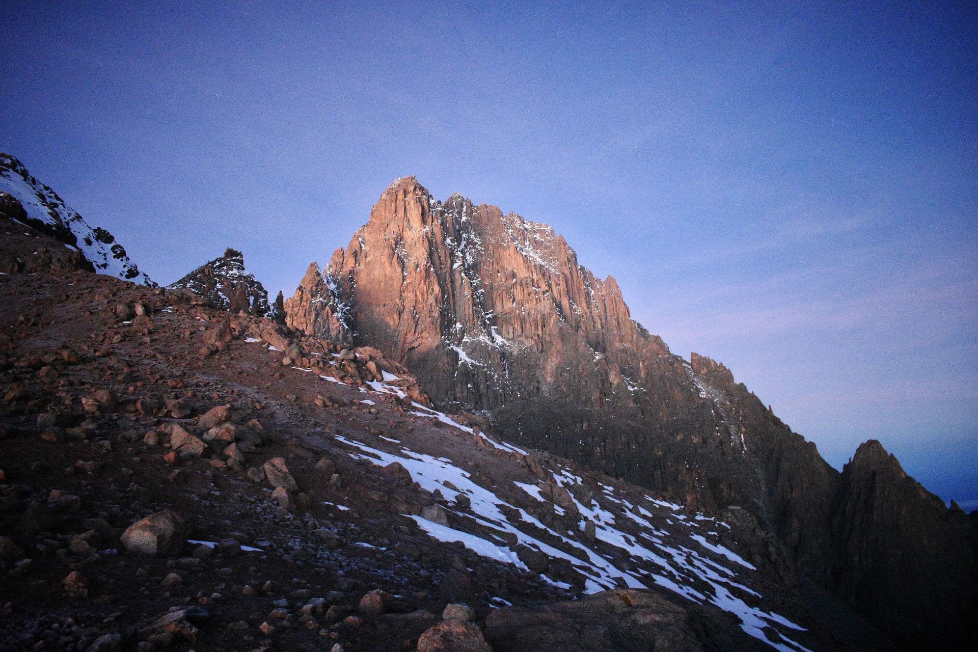 The rocky summit of Batian, Mount Kenya, lit pink at dawn, with snow on the slopes below