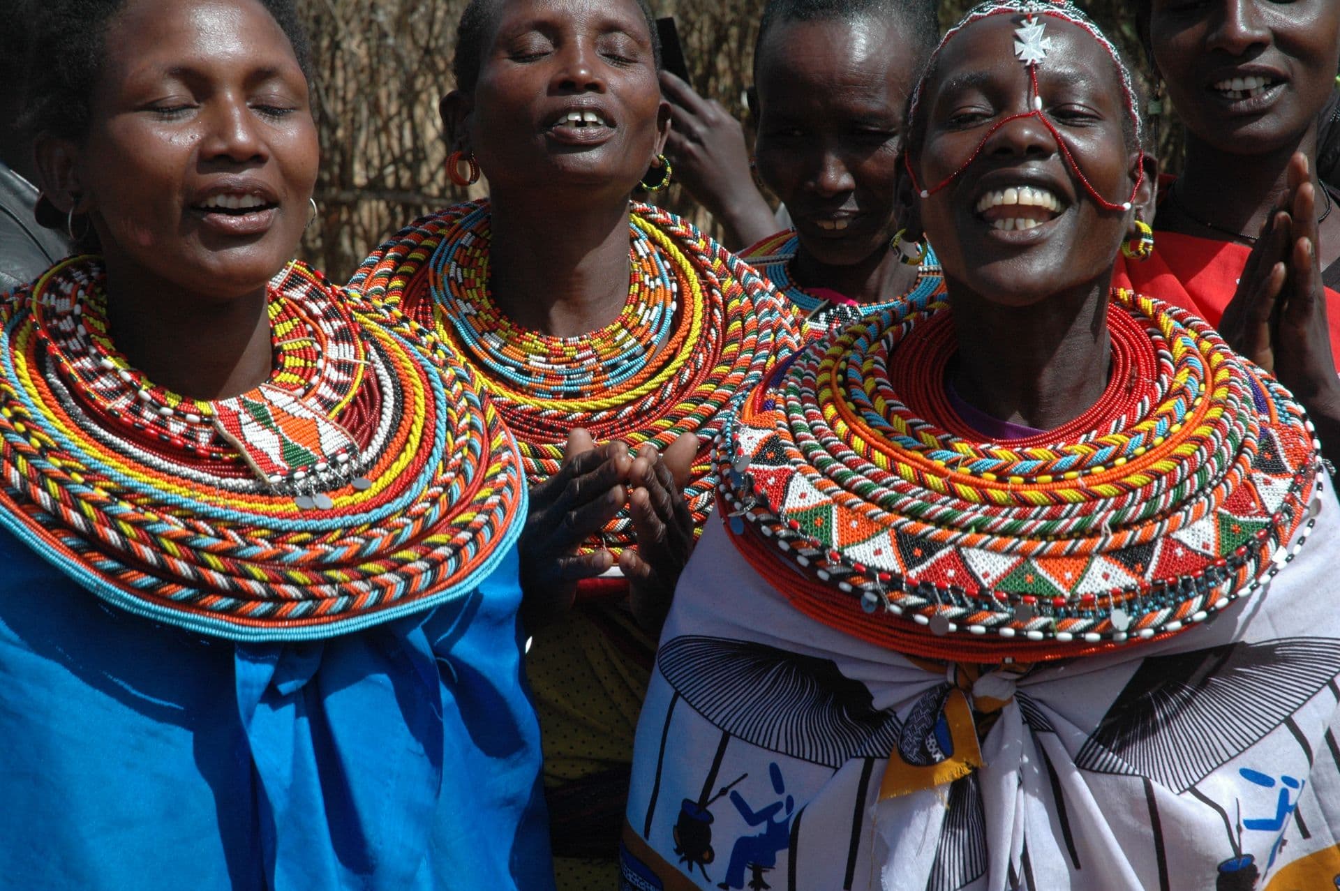 Samburu women in layered red and white beaded necklaces singing and dancing together