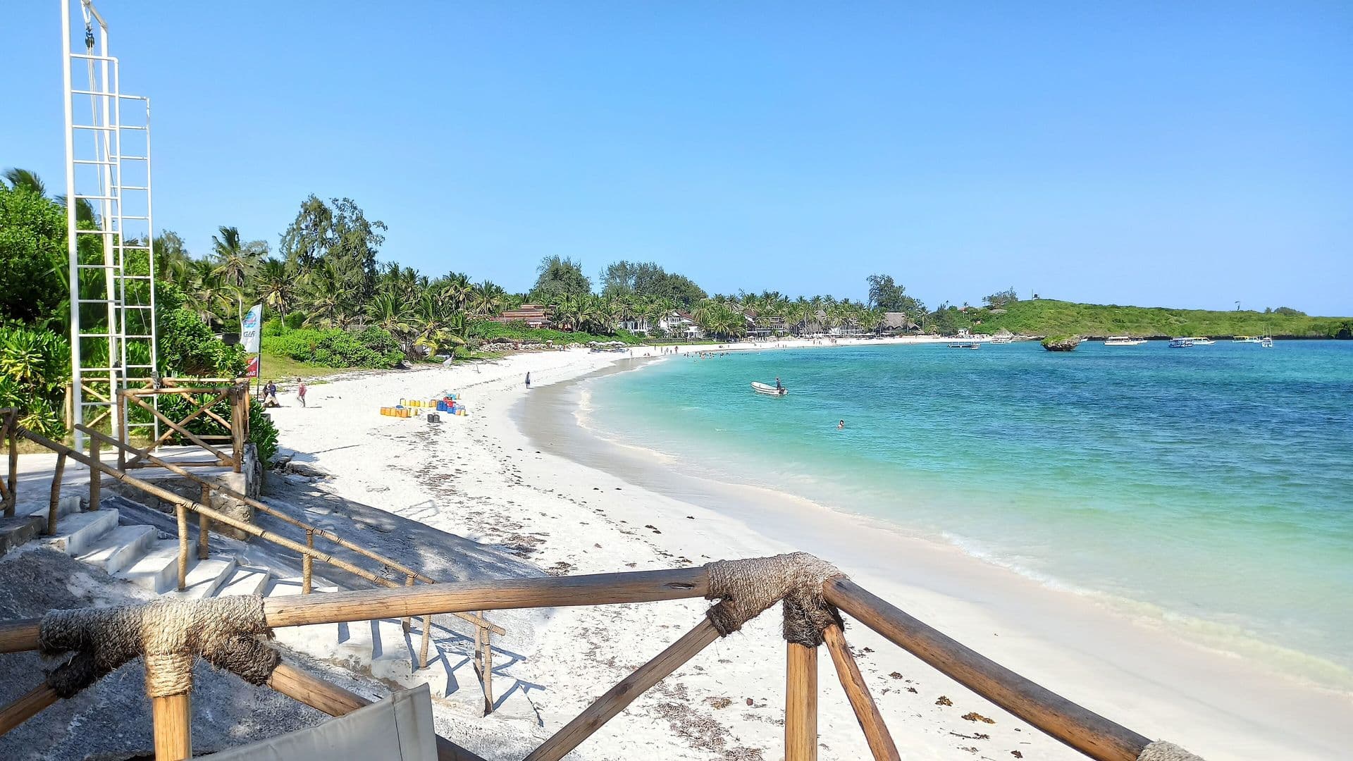 A curved white-sand beach and turquoise water at Watamu, seen from a wooden railing